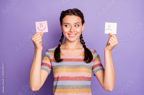 Photo of funny lady holding paper emoticons good and bad mood picking positive emotions wear casual striped t-shirt isolated pastel purple color background photo