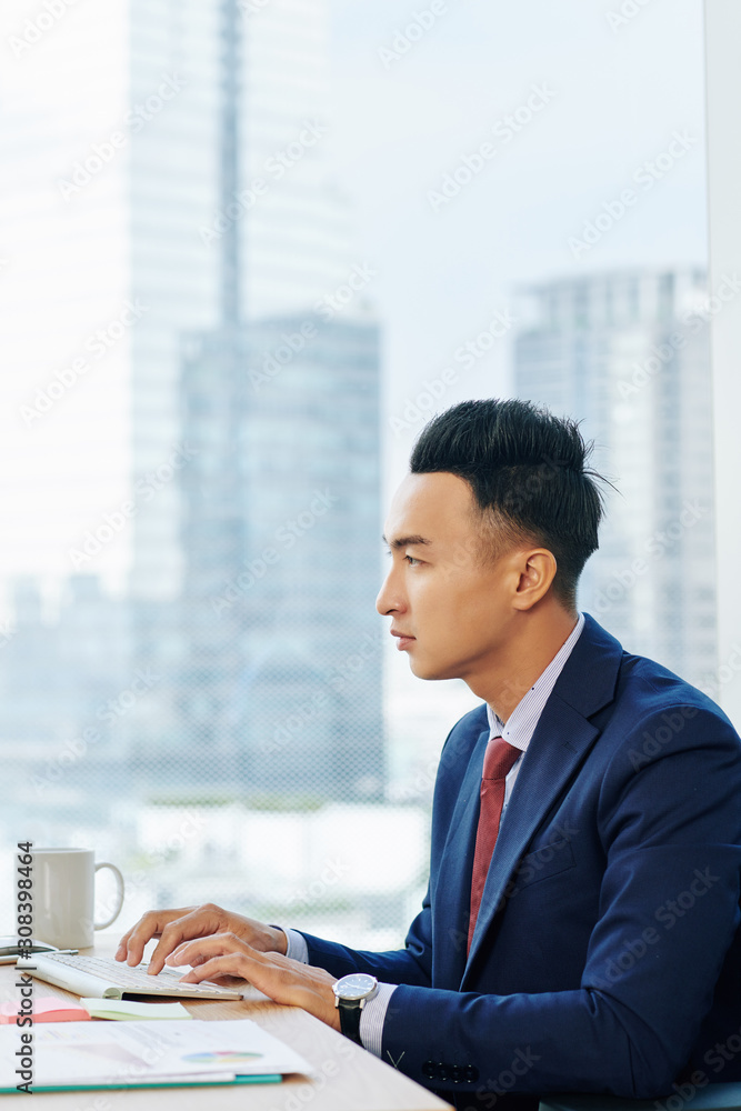 Handsome young Asian businessman concentraed on work. He is typing on computer keyboard and looking at screen Handsome young Asian businessman concentraed on work. He is typing on computer keyboard and looking at screen
