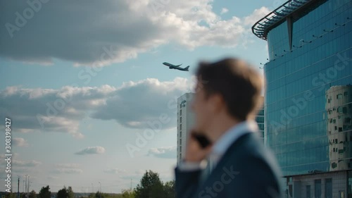 Aircraft taking off on the background. Focus shifting on handsome man dressed formal talking on smartphone. Man seeing off plane waving hand goodbye. Outside terminal