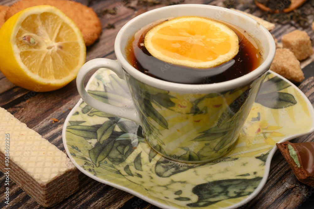 A Cup of black tea, sliced lemon, brown sugar slices, oatmeal cookies, waffles on a wooden background. Close up. A Cup of black tea, sliced lemon, brown sugar slices, oatmeal cookies, waffles on a wooden background. Close up.