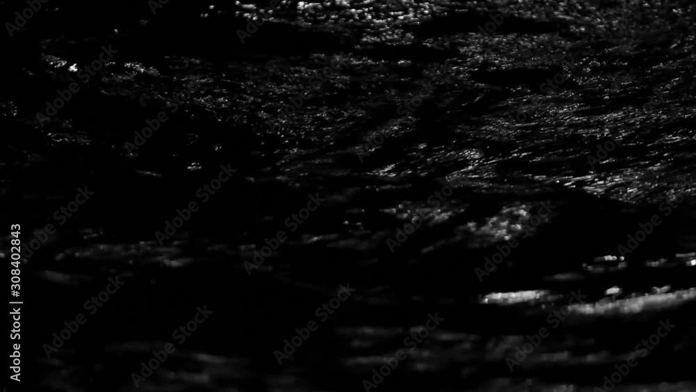 The defocused view of river stream water slowly flowing through natural rock beach at night. Abstract nature background.