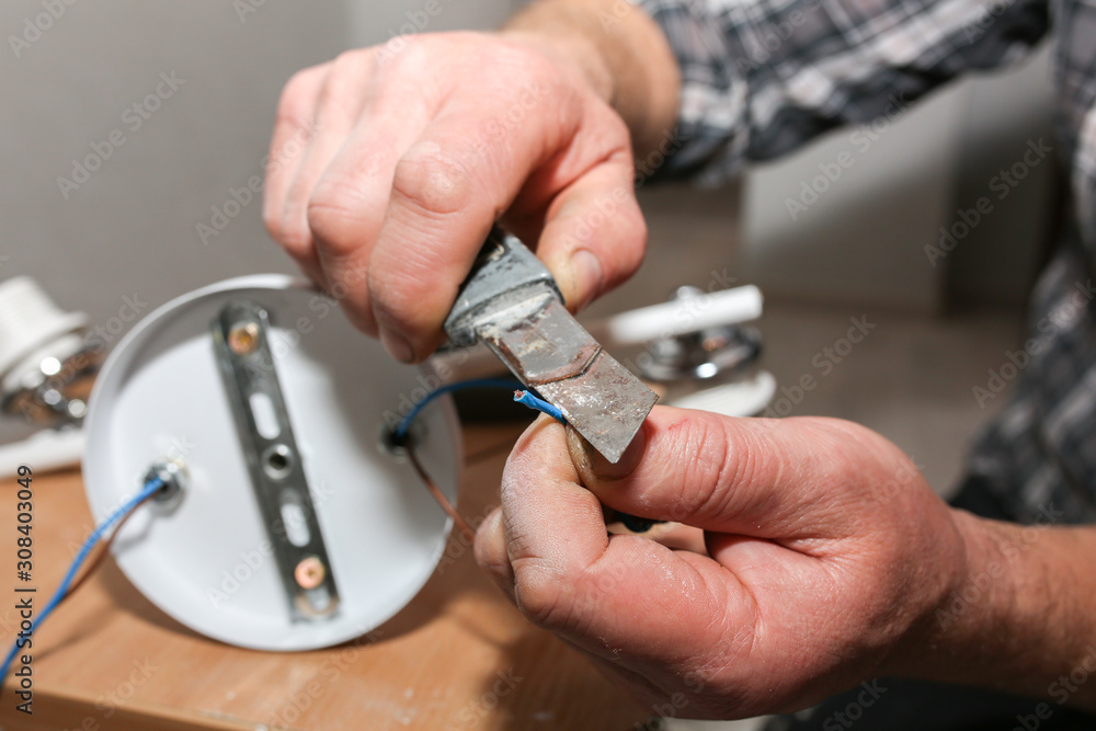Fototapeta premium Man is holding pliers in his hands. Lamp installation. Electrical insulator for light bulb. Restoration indoors.