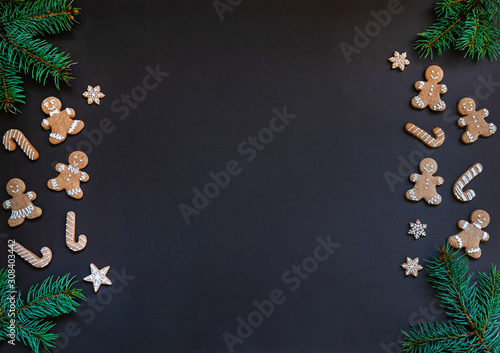 Christmas or winter composition. Border made of gingerbread cookies and spruce branches on dark background. Christmas, winter, new year concept. Flat lay, top view, copy space.