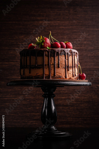 Chocolate cake with with berries, strawberries and cherries. cake on a dark brown background. copy space photo