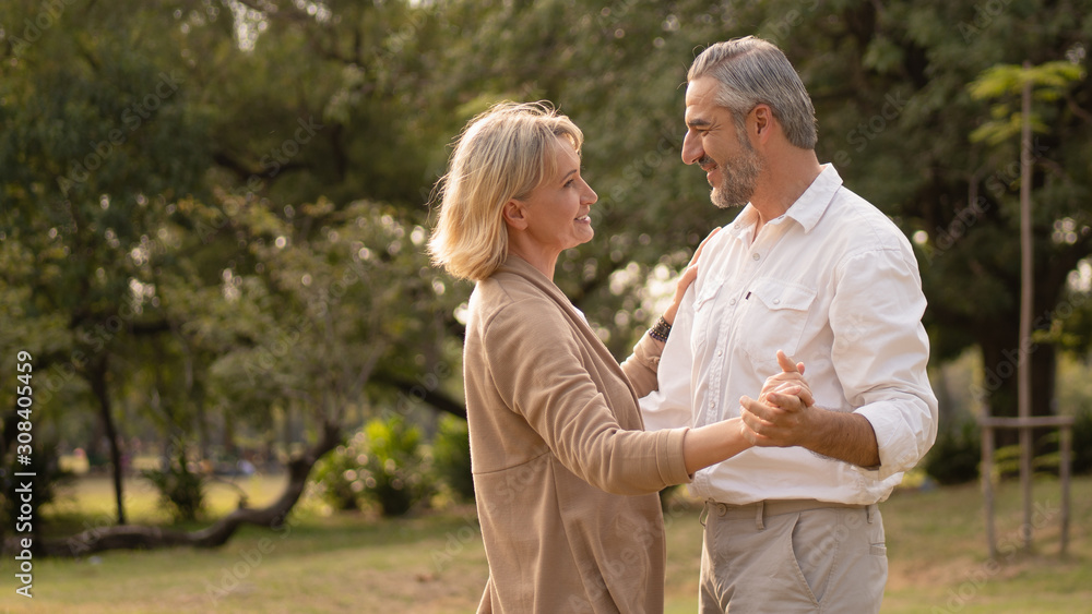 Senior elegant caucasian couple dancing looking at each other feeling love and cherish on their anniversary in the park with copy space, happily retired spouse, well-managed retirement life concept. Senior elegant caucasian couple dancing looking at each other feeling love and cherish on their anniversary in the park with copy space, happily retired spouse, well-managed retirement life concept.