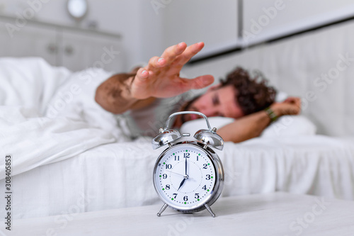 Man lying in bed turning off an alarm clock in the morning at 7am. Hand turns off the alarm clock waking up at morning, man turns off the alarm clock waking up in the morning from a call.