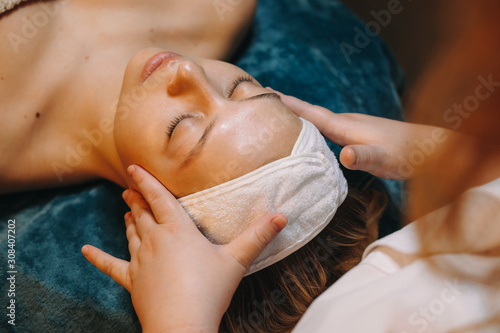 Upper view of a beautiful woman leaning on a spa bed having a facial massage in a wellness spa center. photo