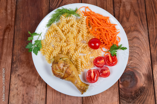 Grilled chicken leg with cooked spiral pasta, vegetables, top view