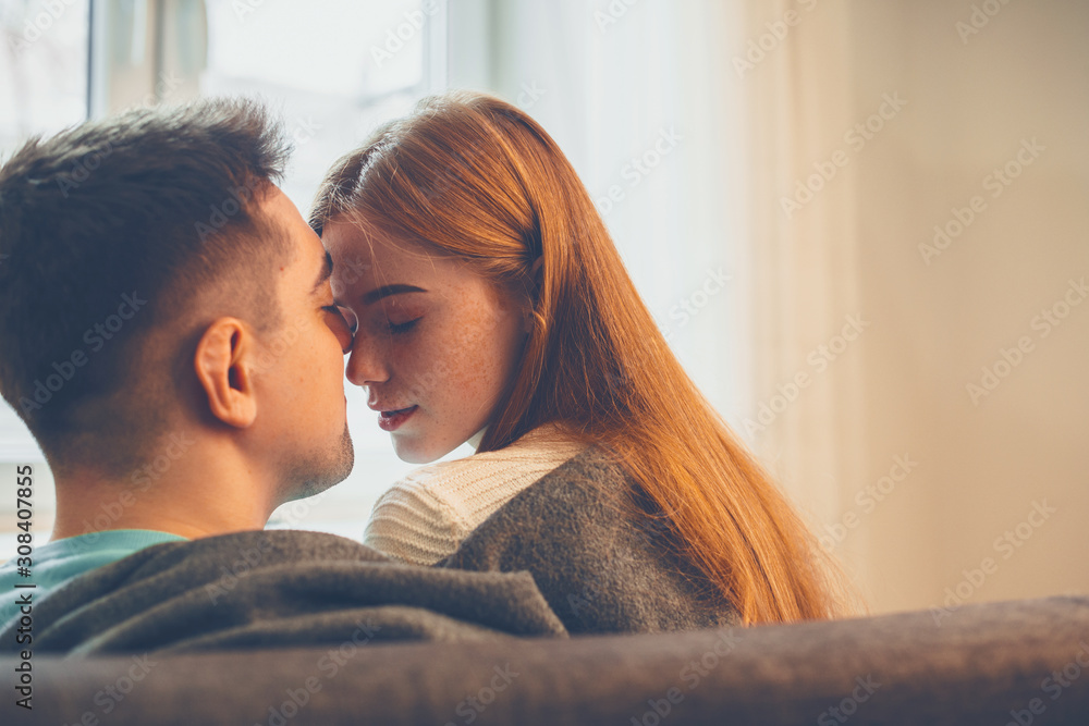 Charming young couple sitting on the couch close face to face before kissing . - obrazy, fototapety, plakaty 