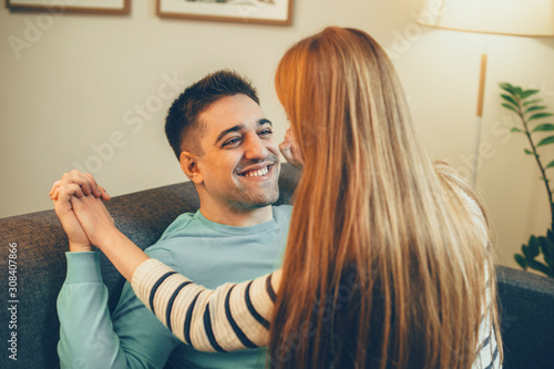 Young man laughing while having fun at couch at home with her girlfriend which is sitting on him.