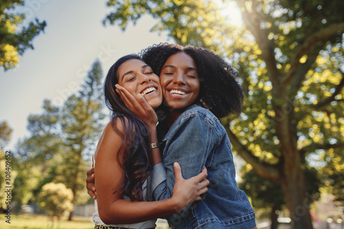 Smiling happy portrait of a diverse young black and white female friends hugging each other and having fun outdoors in the park  photo