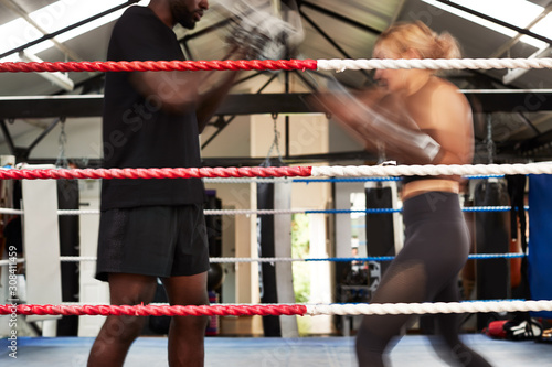 Action Shot Of Male Personal Trainer Sparring With Female Boxer In Gym Using Training Gloves