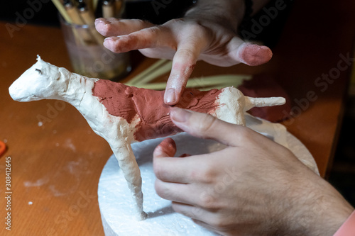 Close-up of male potter hands working on sculpture at table, dog