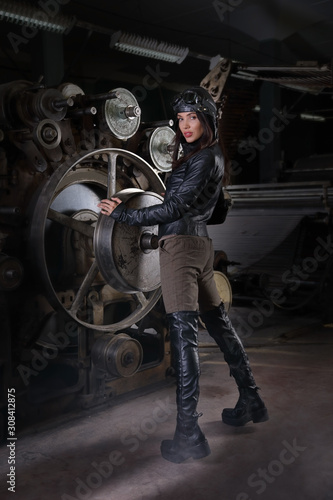 Beautiful girl in a retro pilot costume standing at the machine in the workshop