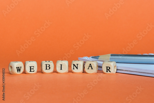 Concept webinar (online workshop, training, internet learning, teaching seminar education)  Wooden Blocks with the text: Webinar.  notebook and pencil. Orange background, copy space