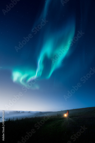 a man with a lantern walking on a field at night with aurora on the sky