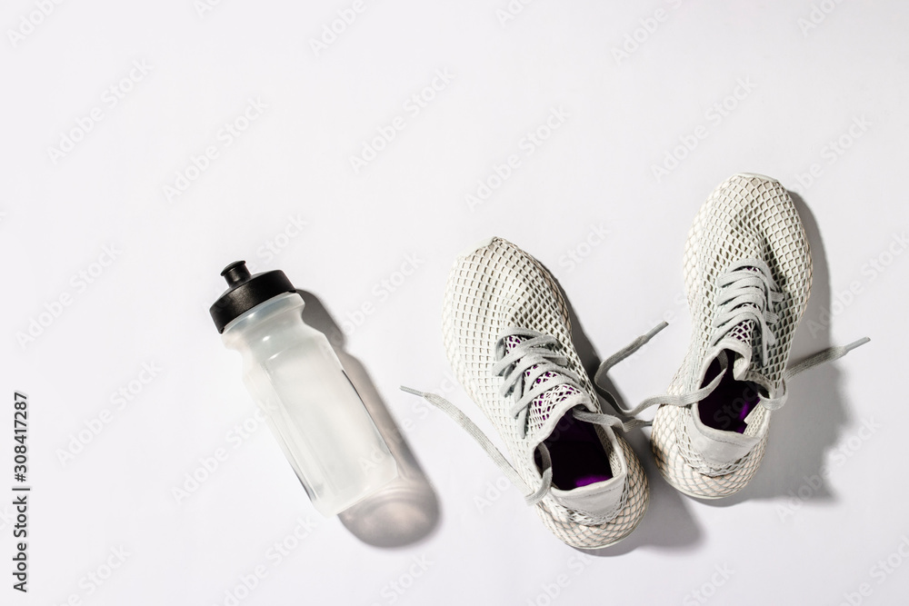White sneakers and a bottle with water under morning sunlight on a white background. Concept, jogging, running, fitness, cross fit. Morning run. Banner. Flat lay, top view - obrazy, fototapety, plakaty 