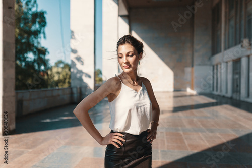 Smiling pretty woman holding hands on the hips while posing in the city