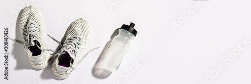 White sneakers and a bottle with water under morning sunlight on a white background. Concept, jogging, running, fitness, cross fit. Morning run. Banner. Flat lay, top view