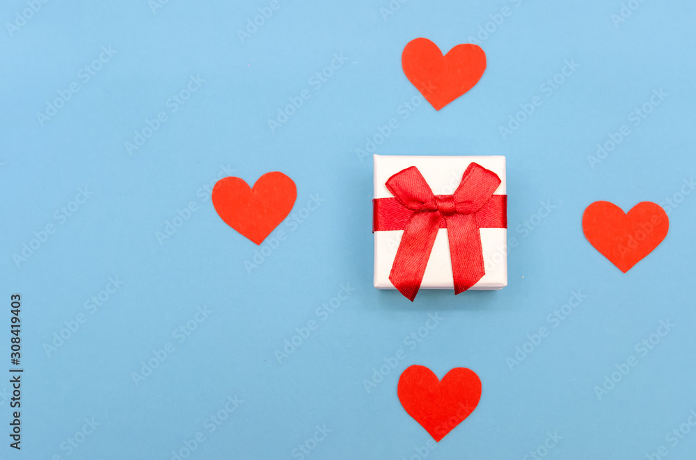 Gift box among red paper hearts on a blue background. Top view, copy space. Valentine's day, a symbol of love. Festive background