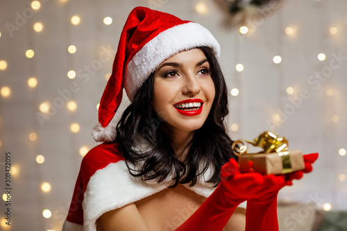 beautiful sexy girl wearing santa claus clothes with christmas gift box on the background of the Christmas lights