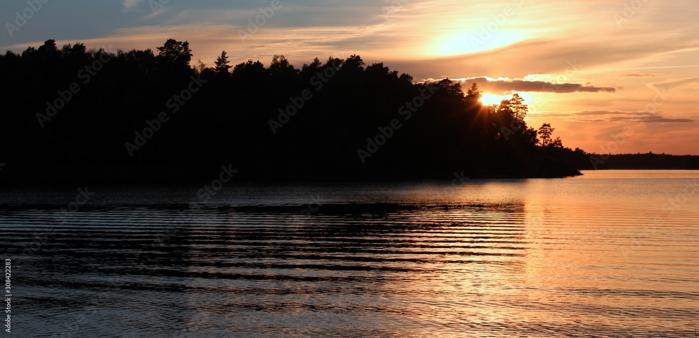 Fototapeta premium glowing evening sun behind the forest on a fjord