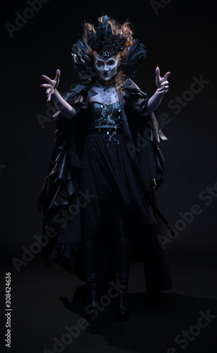 Portrait of woman witch in black clothes conjures on the dark background