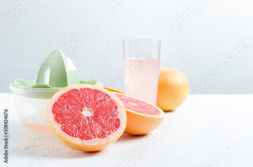 Closeup of cut grapefruit, manual juicer and glass of grapefruit juice on the white table against white wall