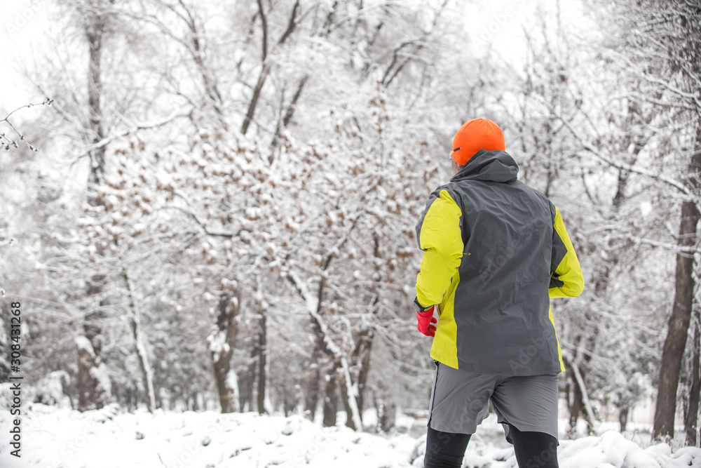 Man running in the forest in winter time. Man wearing sportswear at winter in park 