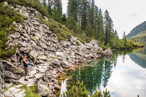 Woman tourist sitting on stone looking at Morskie Oko lake, Tatra Mountains, Poland