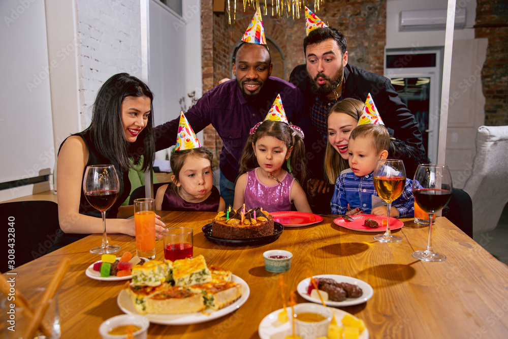 Portrait of happy multiethnic family celebrating a birthday at home. Big family eating snacks and drinking wine while greeting and having fun children. Celebration, family, party, home concept.