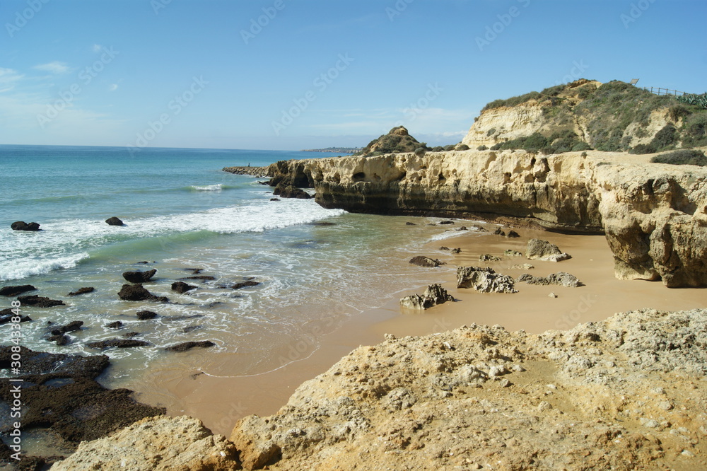 A beautiful rocky small bay near the Portuguese seaside resort of Albufeira on the Algarve coast.  Atlantic waves break on the broad sandy beach.  Blue skies - copy space.