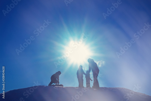 People ride a snow slide on a tuba and sled, silhouettes against the sun
