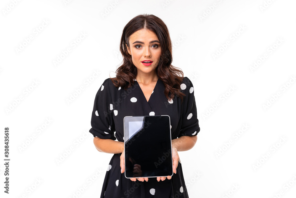 Young girl with delightful smile, in black and white dress in peas shows a tablet, picture isolated on white background Young girl with delightful smile, in black and white dress in peas shows a tablet, picture isolated on white background