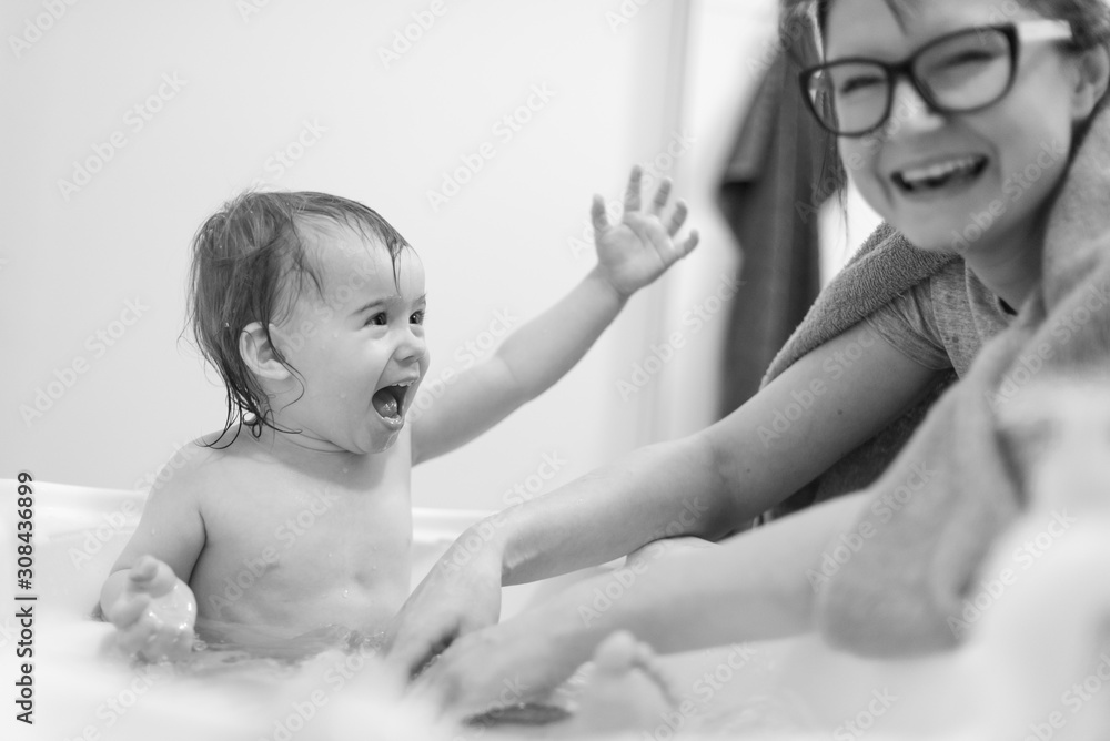 Happy 1 year old Baby in bathtub taking bath in bathroom with mother