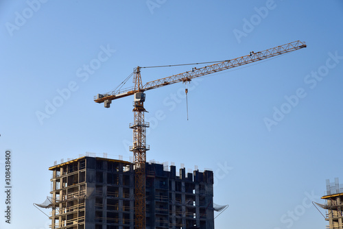 Tower cranes constructing a new residential building at a construction site against blue sky. Renovation program, development, concept of the buildings industry.