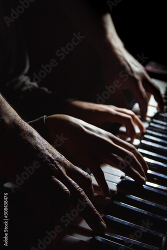 playing four male hands on the piano. palms lie on the keys and play the keyboard instrument in a music school. student learns to play. hands of a pianist. black dark background.