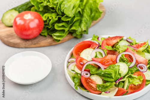 Healthy vegetarian dish on table, vegetable salad with fresh tomato, cucumber, lettuce, red onion on gray concrete background. Diet menu. mockup, template