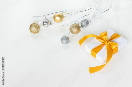 Paper gift box wrapped with yellow ribbon and champagne glasses filled with Christmas decorations, isolated on white background. Presents and holidays concept.