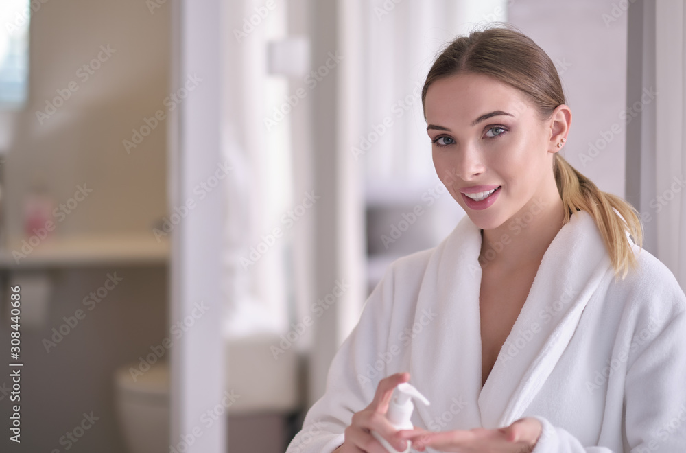 Beautiful young woman after bath applying body cream onto skin at home Beautiful young woman after bath applying body cream onto skin at home