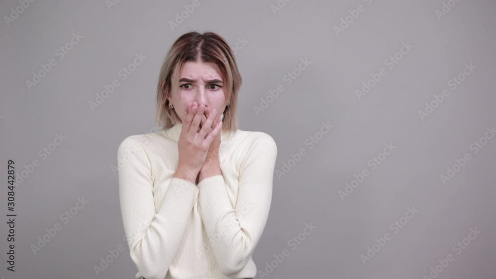 Young attractive blonde woman wearing white clothes, over isolated gray wall with surprise facial expression, covering mouth with hands Young attractive blonde woman wearing white clothes, over isolated gray wall with surprise facial expression, covering mouth with hands