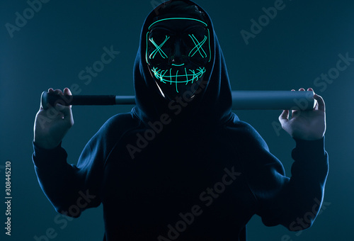 Anonymous criminal man with baseball bat in a black hoodie and neon mask photo