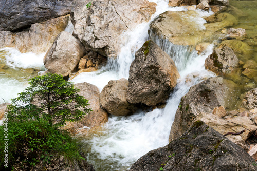 A small fir tree on a steep bank grows near a waterfall.