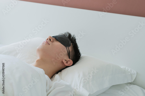 asian young man sleeping in bed with an eye mask in bedroom