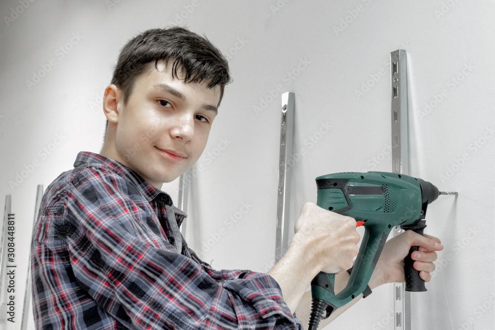 A teenager works as a builder, holding a drill or perforator. Concept of child labour, choice of profession A teenager works as a builder, holding a drill or perforator. Concept of child labour, choice of profession