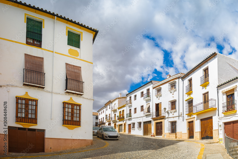 A small narrow street with white houses and cars in the old European city. Ronda, Andalusia, Spain. Panorama