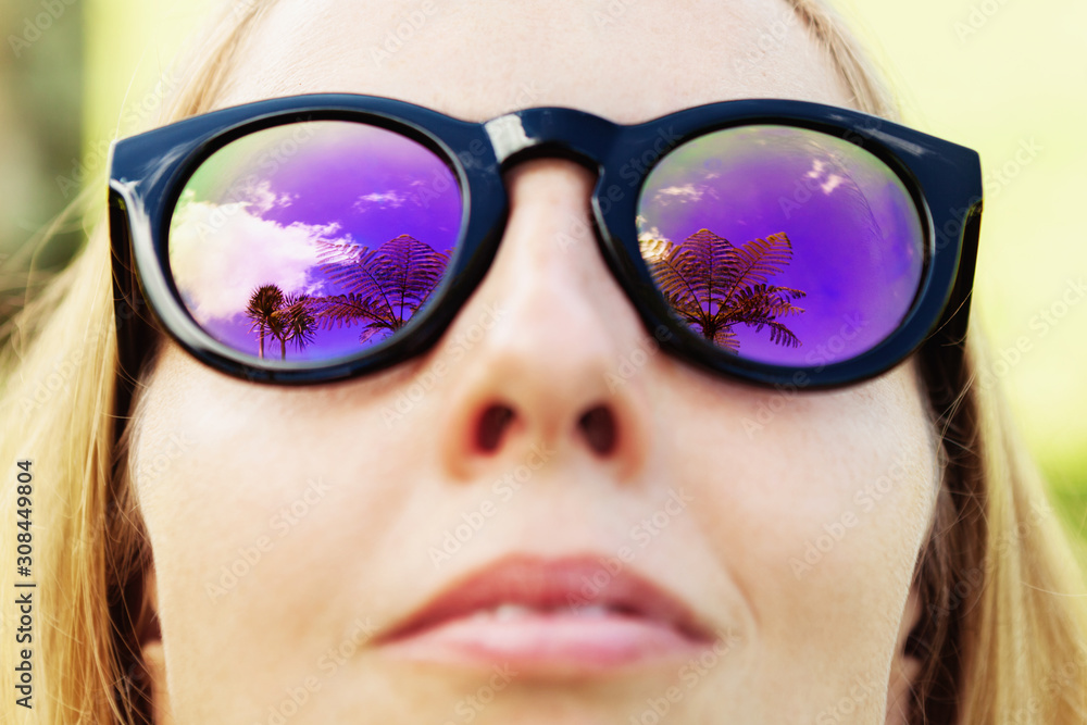 Woman wearing sunglasses with palms, sky reflection in mirror lens Woman wearing sunglasses with palms, sky reflection in mirror lens