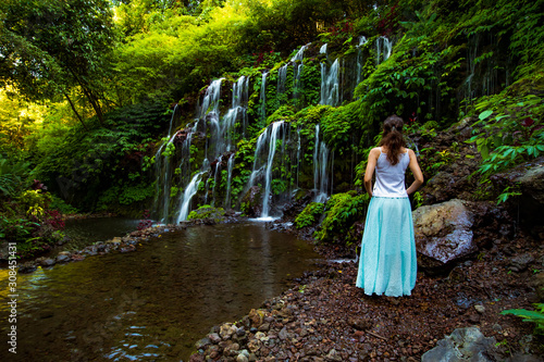 Young traveler woman at waterfall in tropical forest. View from back. Banyu Wana Amertha waterfall Wanagiri, Bali. Slow shutter speed, motion photography. photo