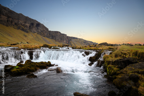 Panoramic summer view of small waterfall near Bjodvegur road. Wonderful sunrise on Iceland, Vik location. Beauty of nature concept background..