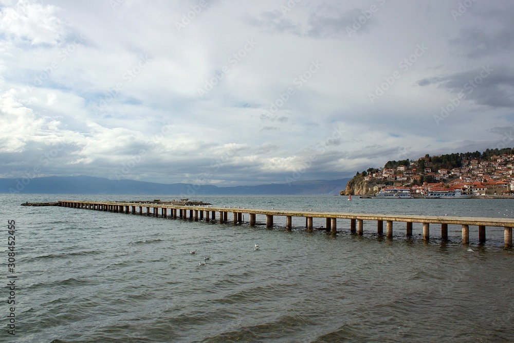  Ohrid lake wooden pier and Ohrid city at the background in North Macedonia in Europe at winter in a cloudy day